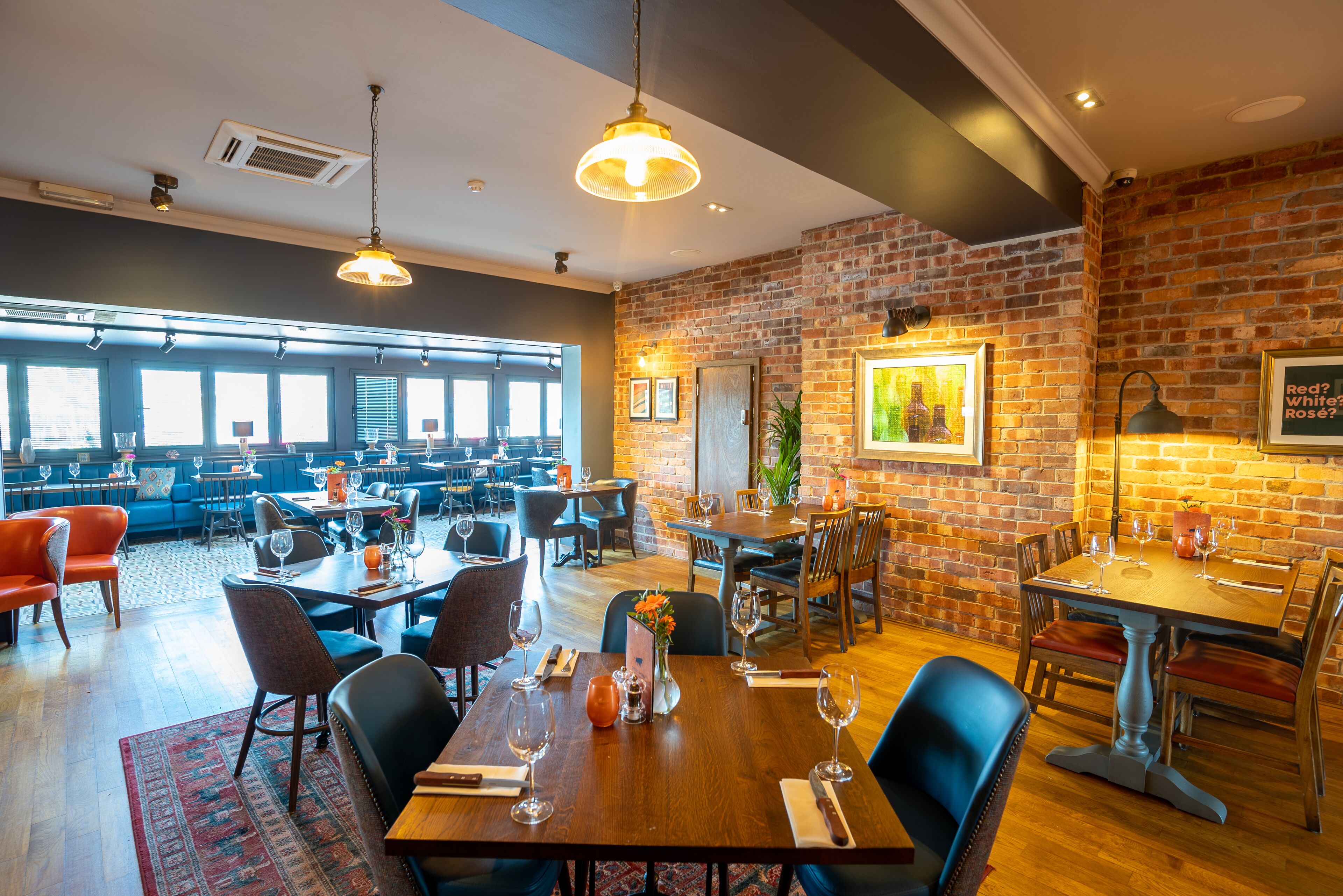 Een restaurant met meerdere eettafels en stoelen, een bakstenen muur en grote ramen.