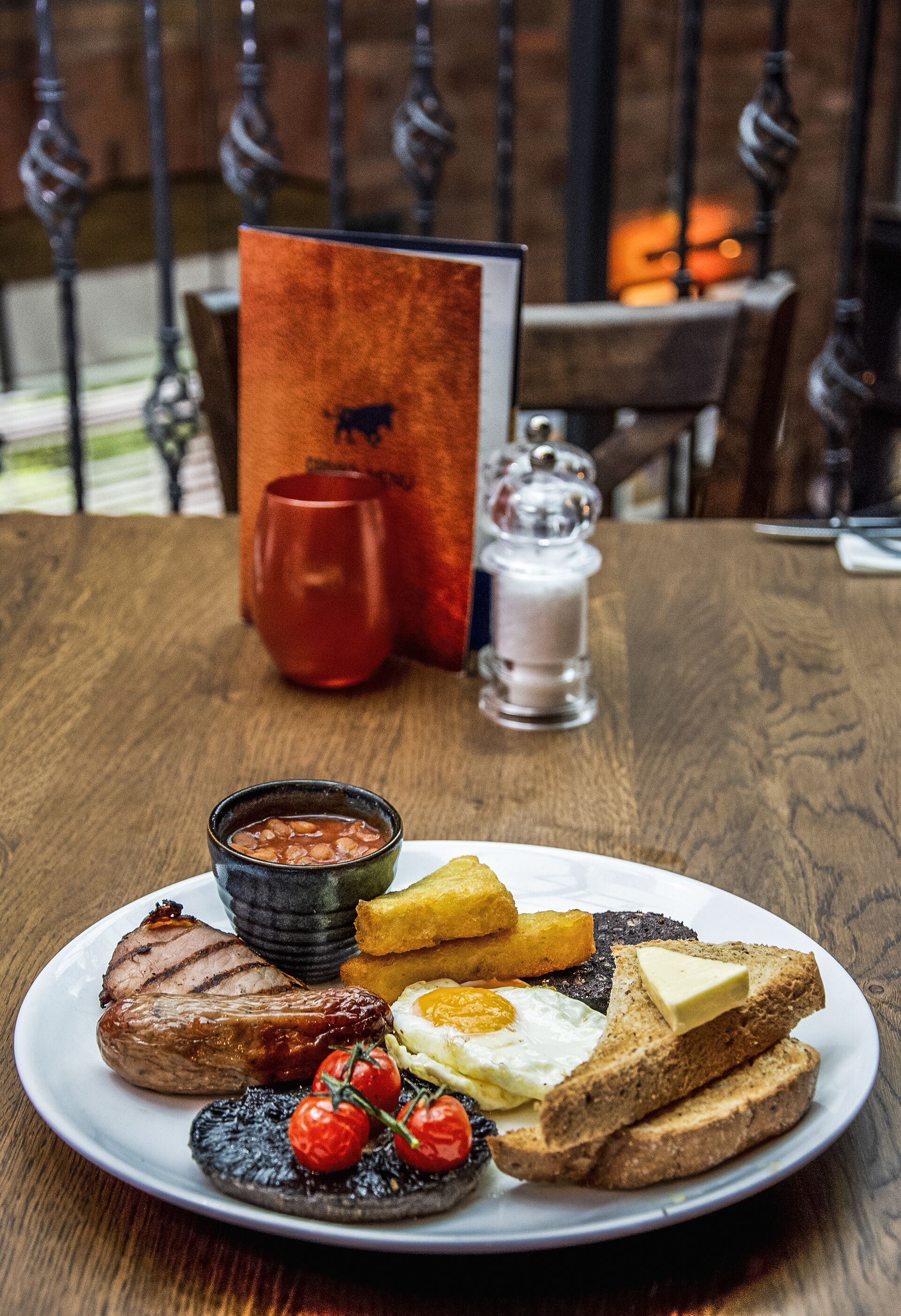 Un plato de desayuno con huevos, tocino, tostadas y tomates sobre una mesa de madera.