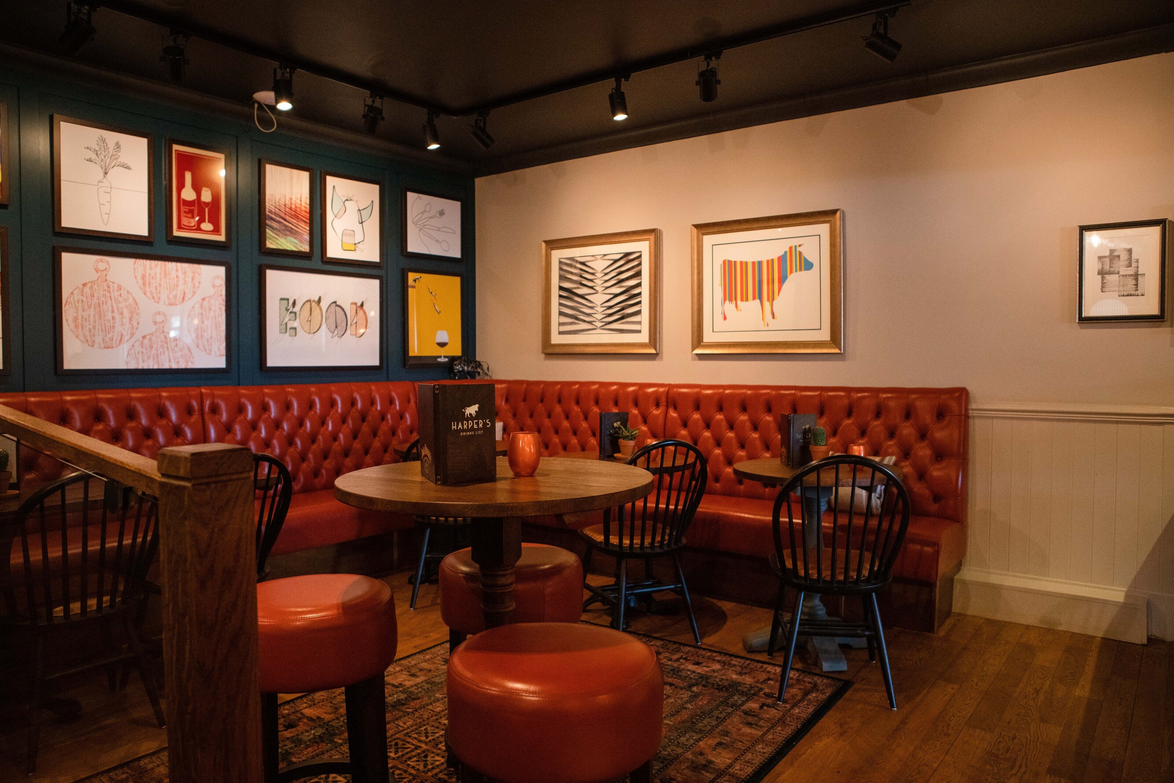 Interior de restaurante con asientos de cuero rojo, mesas y sillas de madera. Se observan obras de arte enmarcadas en las paredes.