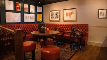 Interior de restaurante con asientos de cuero rojo, mesas y sillas de madera. Se observan obras de arte enmarcadas en las paredes.
