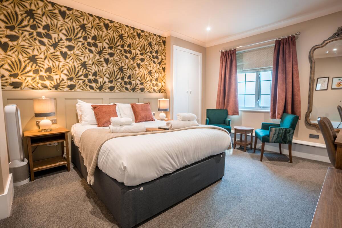 A bedroom with a large bed, a nightstand, a chair, and a window with curtains.