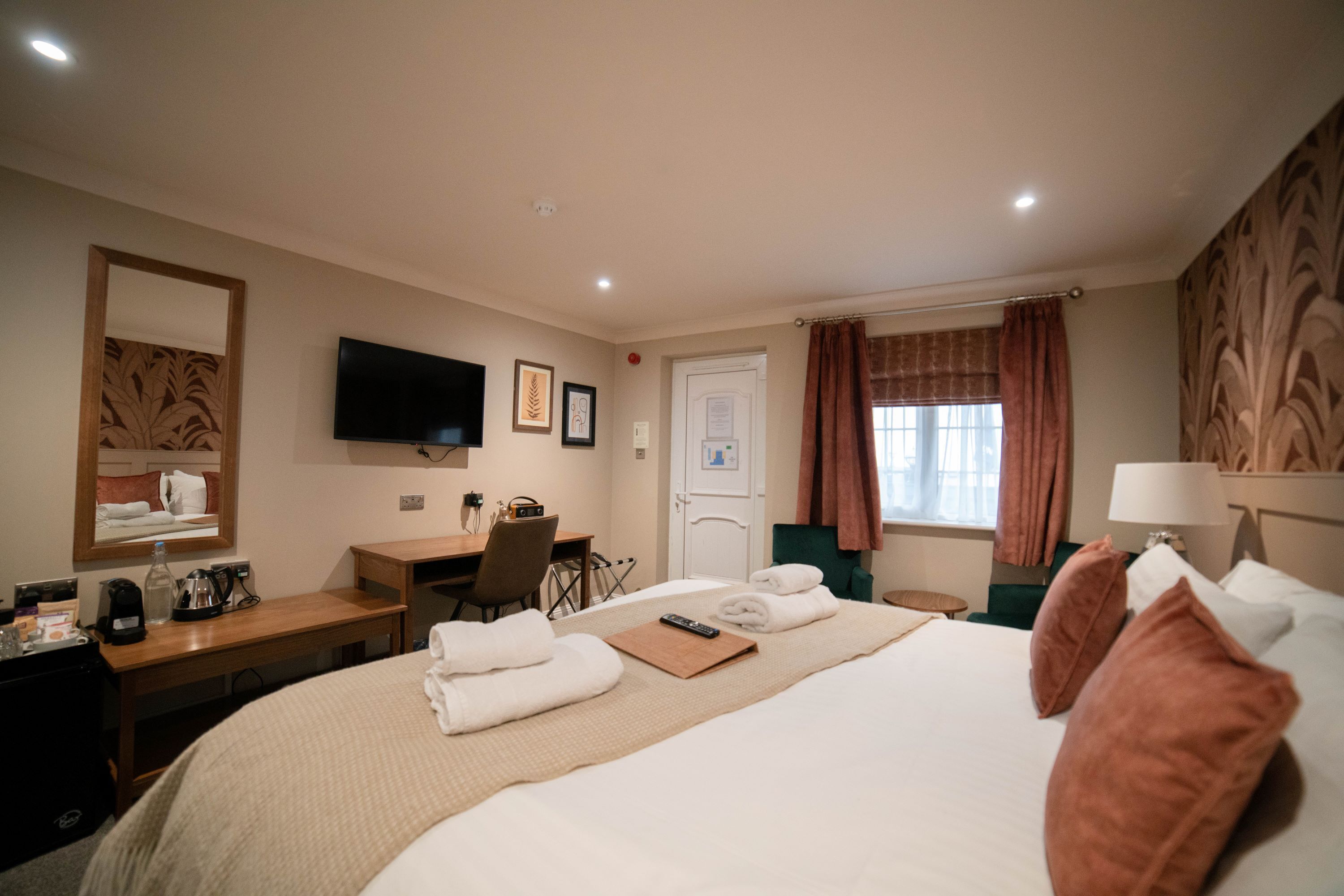 Habitación de hotel con cama, escritorio, silla, televisión y ventana con cortinas.