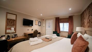 Habitación de hotel con cama, escritorio, silla, televisión y ventana con cortinas.