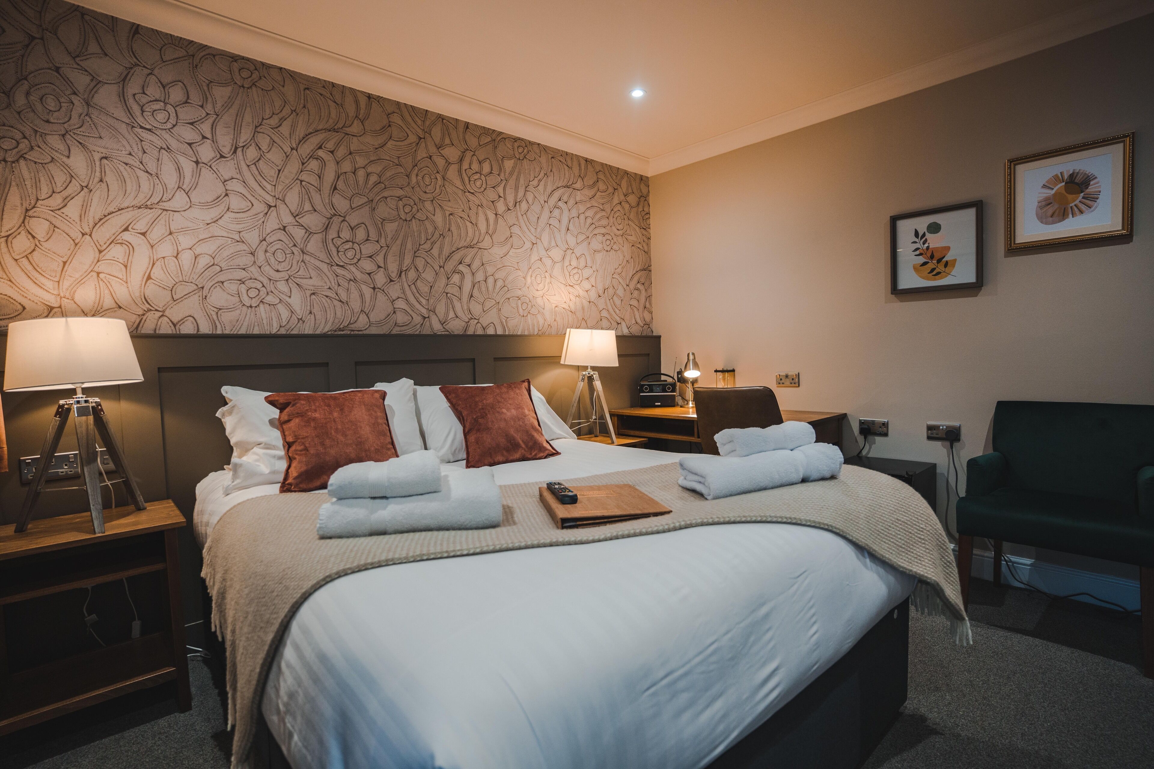 A neatly made bed with white and brown pillows, a bedside lamp, and a bedside table with a lamp.