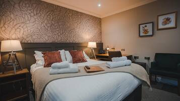 A neatly made bed with white and brown pillows, a bedside lamp, and a bedside table with a lamp.