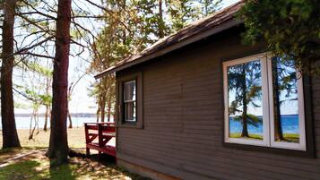 A cabin with a view of the lake, a bench, and a window reflecting trees.