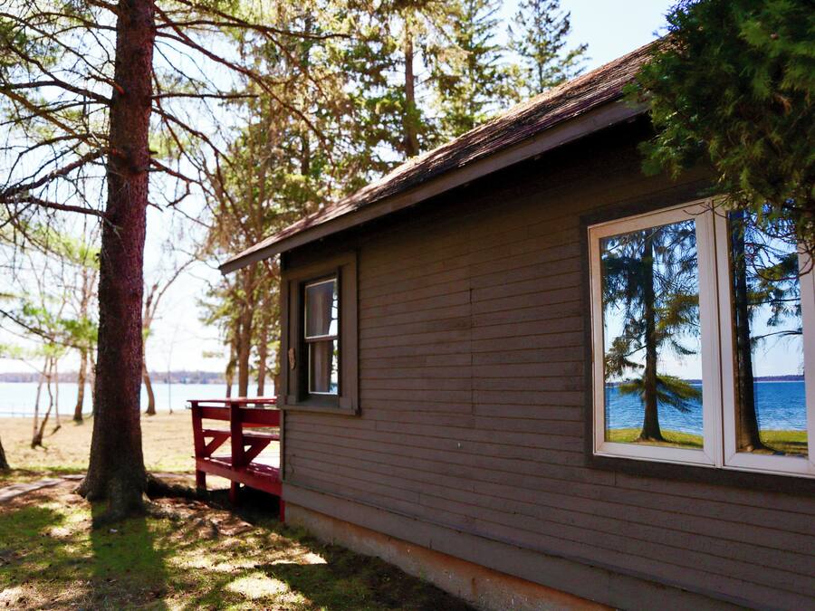 A cabin with a view of the lake, a bench, and a window reflecting trees.