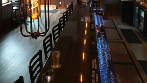 A bar area with hanging industrial-style light fixtures, a long counter with glasses and bottles, and a wooden ceiling. - Ruttger's Birchmont Lodge (Bemidji)