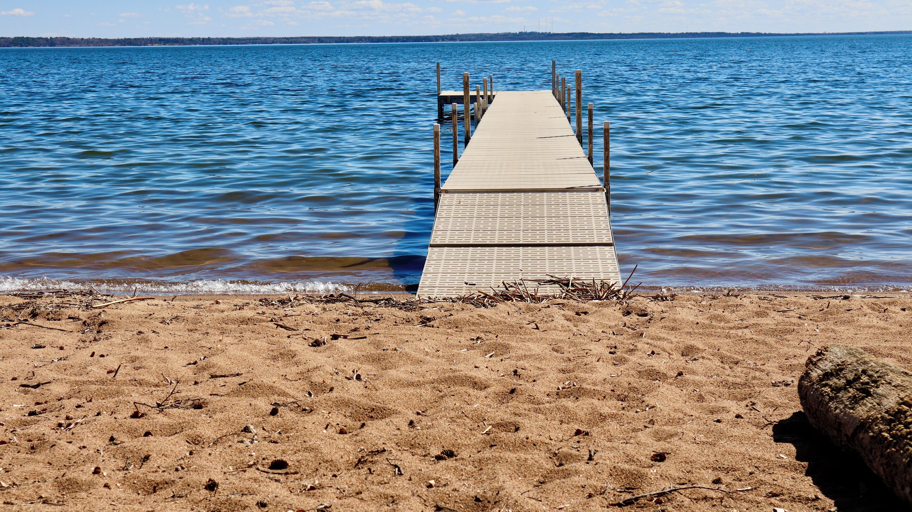 Un muelle de madera se extiende sobre una superficie acuática tranquila, que da a una playa arenosa.