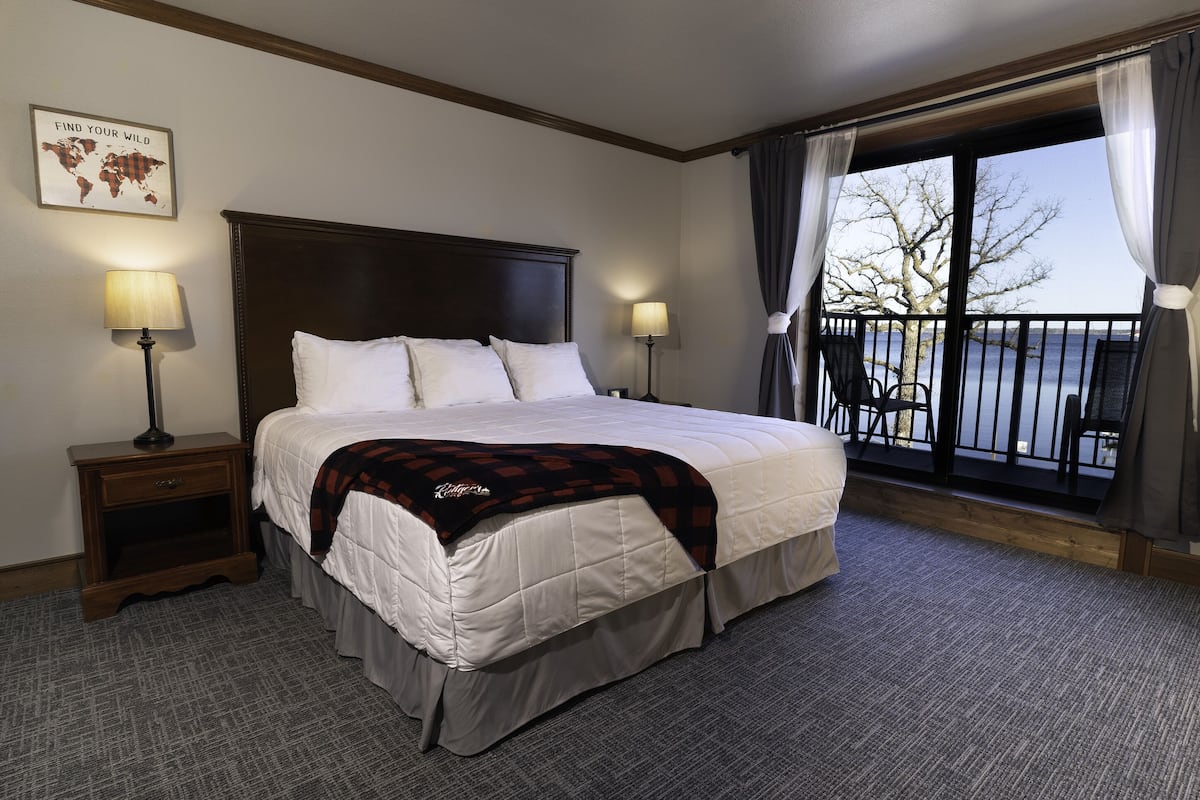 Een hotelkamer met een groot bed, twee nachtkastjes met lampen, een wereldkaart aan de muur, en een balkon met stoelen.