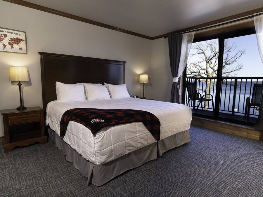 Une chambre d’hôtel avec un grand lit, deux tables de chevet avec des lampes, une carte du monde accrochée au mur et un balcon avec des chaises.