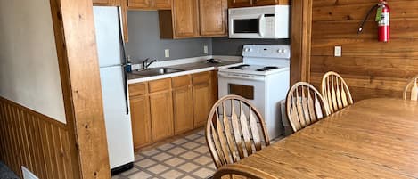 A compact kitchen with wooden cabinets, a microwave, stove, and a dining table with chairs.