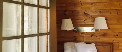 A bedroom with a wooden wall, a bed with white bedding, a ceiling fan, and two wall-mounted lamps.