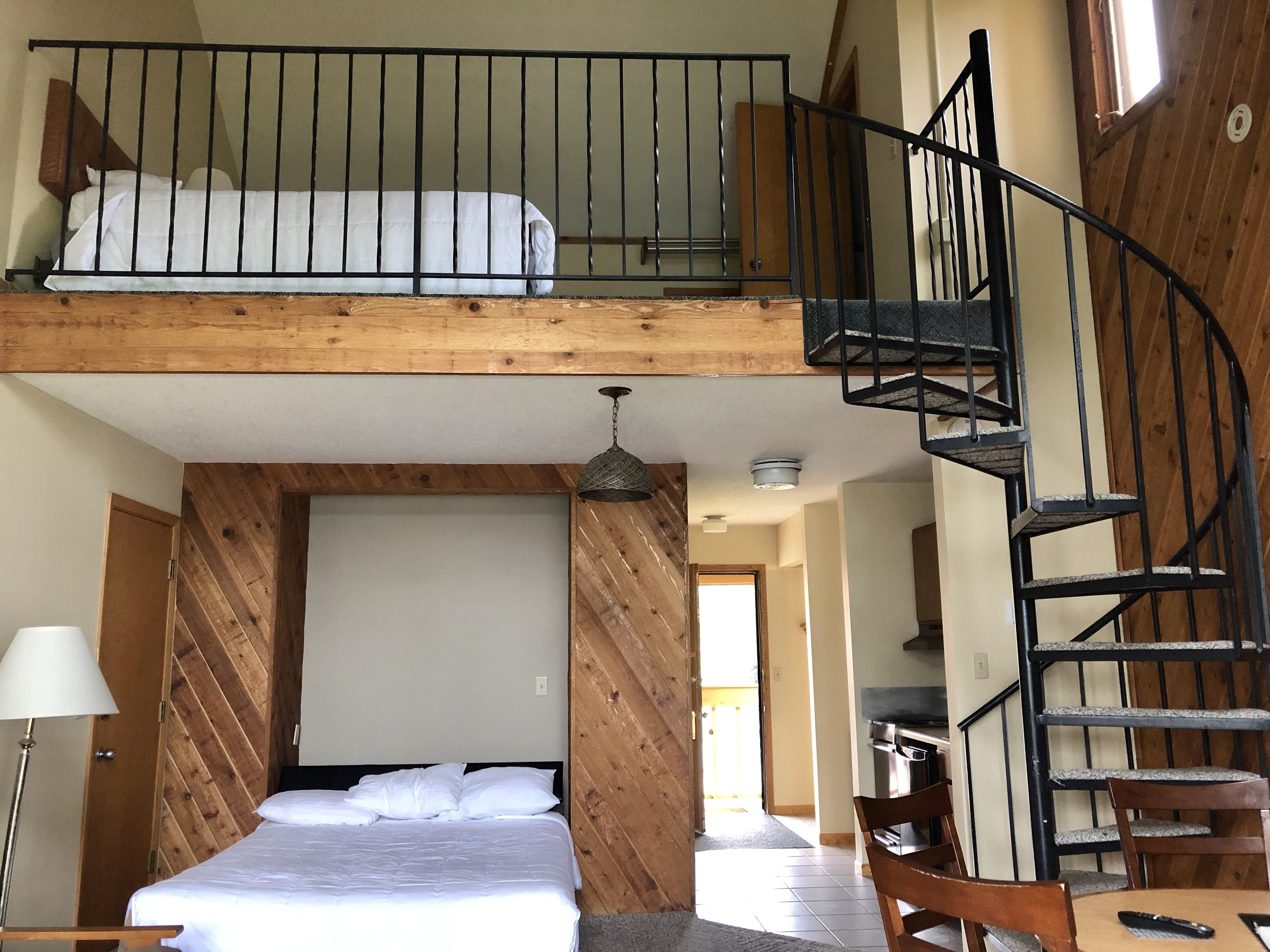 A room with a loft bed, a wooden staircase, and a dining area.
