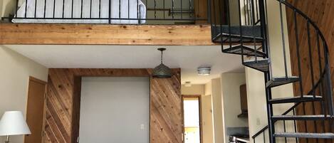 A room with a loft bed, a wooden staircase, and a dining area.