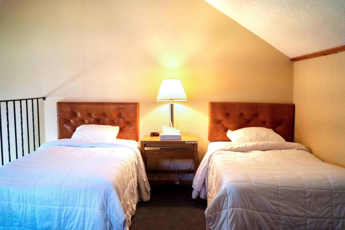Een hotelkamer met twee enkele bedden, een nachtkastje met een lamp en een houten hoofdeinde.