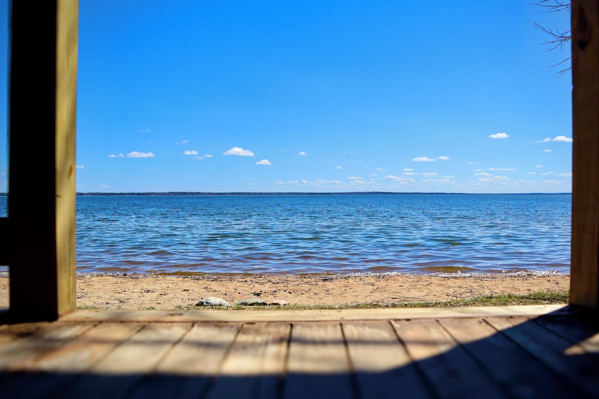 Een houten terras dat naar een strand leidt, met uitzicht op zee en een heldere lucht.