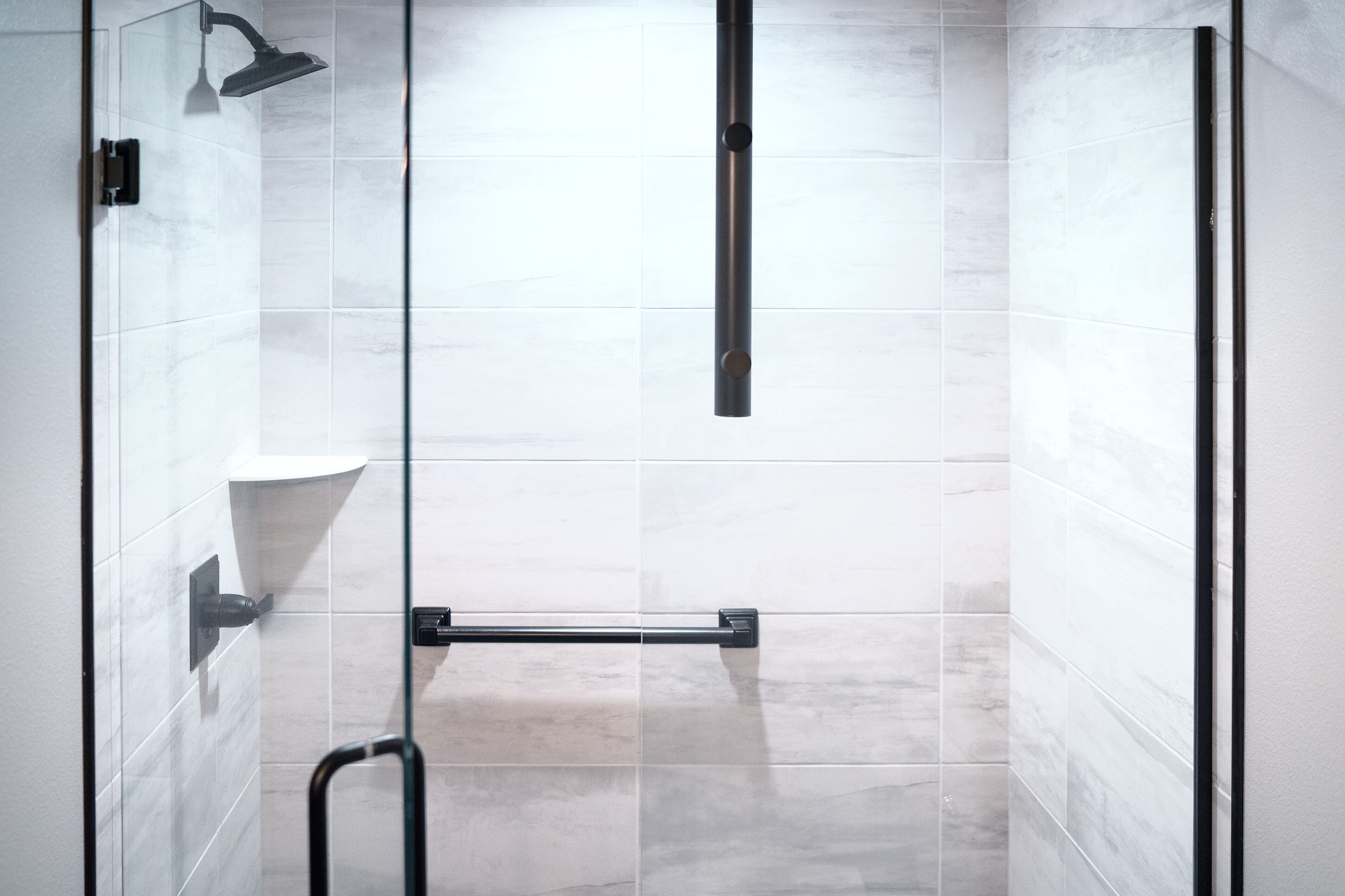 A modern shower with a glass door, a handheld showerhead, and a towel rack.