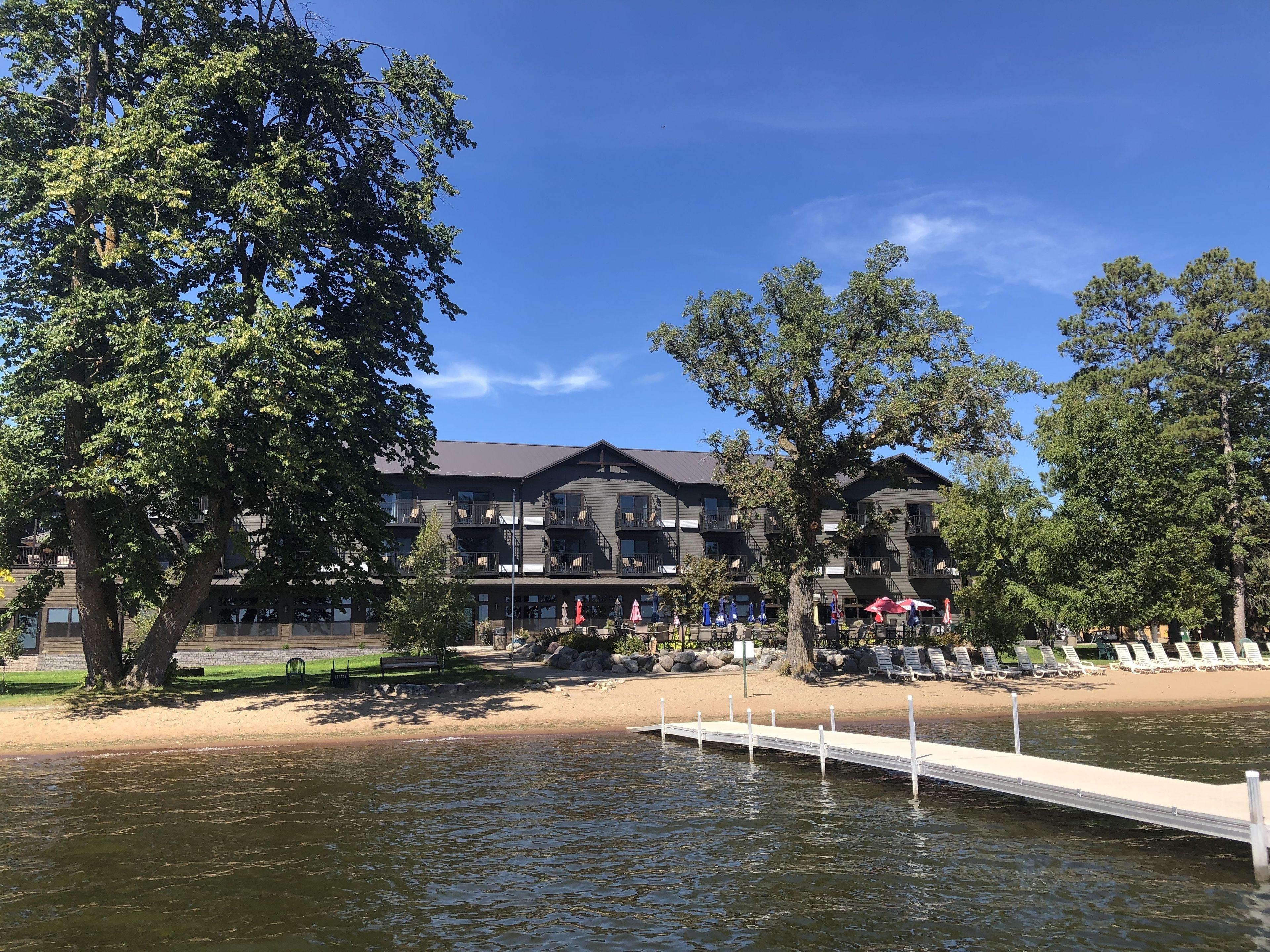 Un hôtel situé au bord d’un lac, doté d’une jetée qui s’avance sur l’eau, entouré d’arbres et bordé d’une plage de sable.