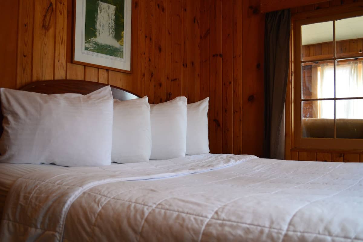 Een bed met wit beddengoed en een houten hoofdeinde in een kamer met houten wanden en een raam met gordijnen.