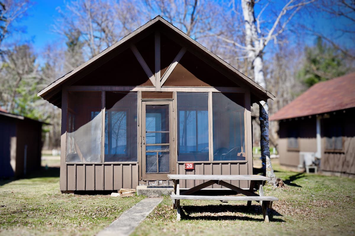 Een klein houten vakantiehuisje met een voordeur en een picknicktafel ervoor.