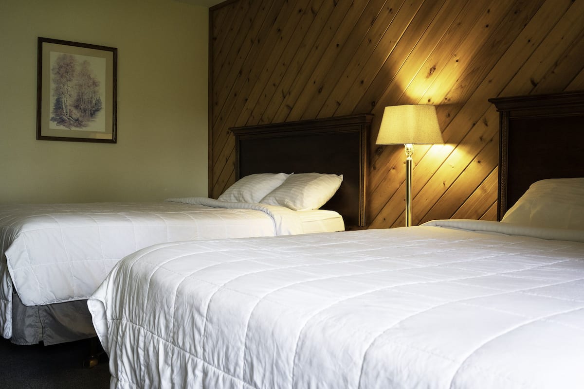 Een hotelkamer met twee bedden, een houten plafond en een ingelijste foto aan de muur.