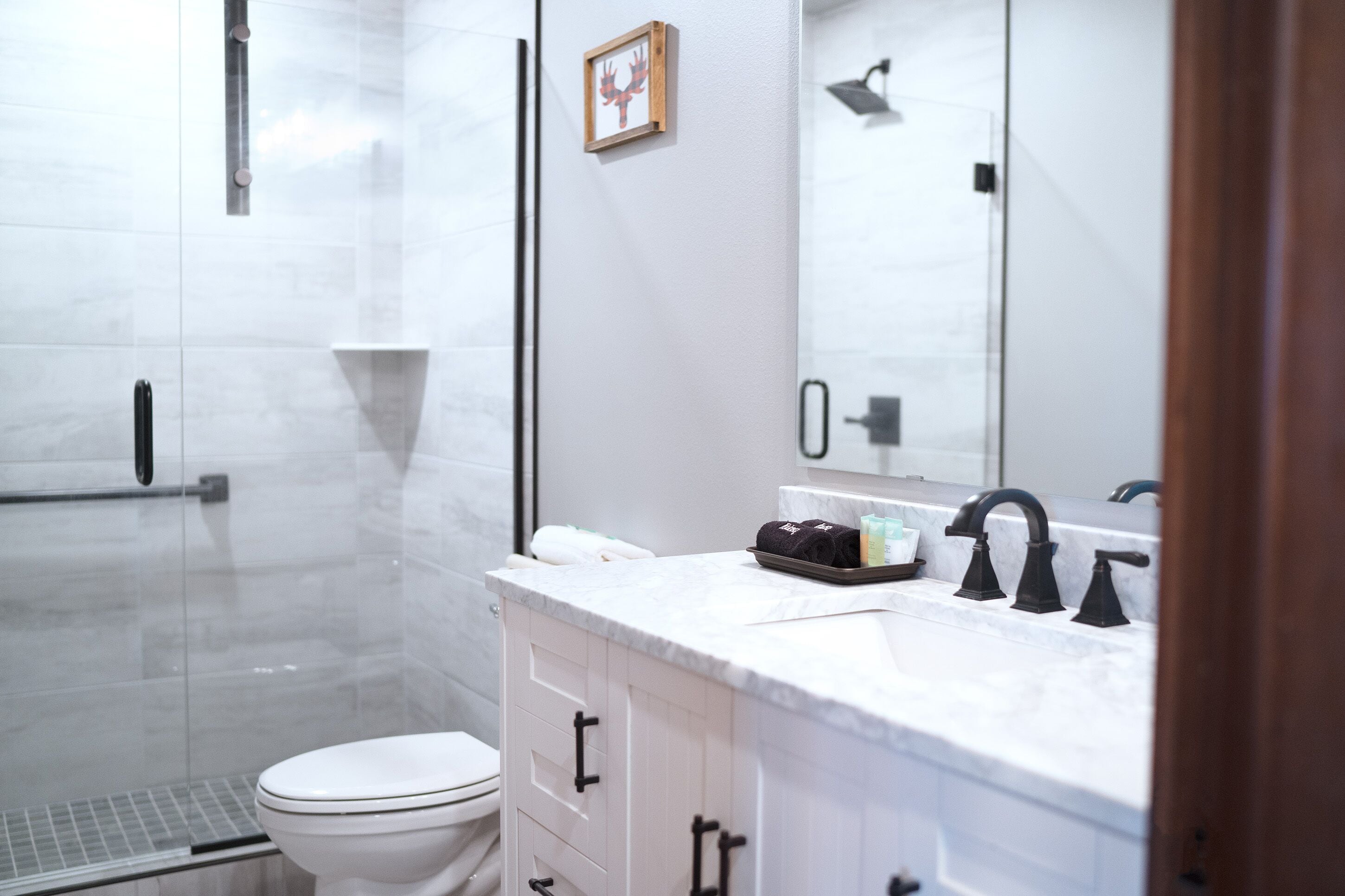A modern bathroom with a glass shower enclosure, a white toilet, a marble sink, and a mirror above the sink.
