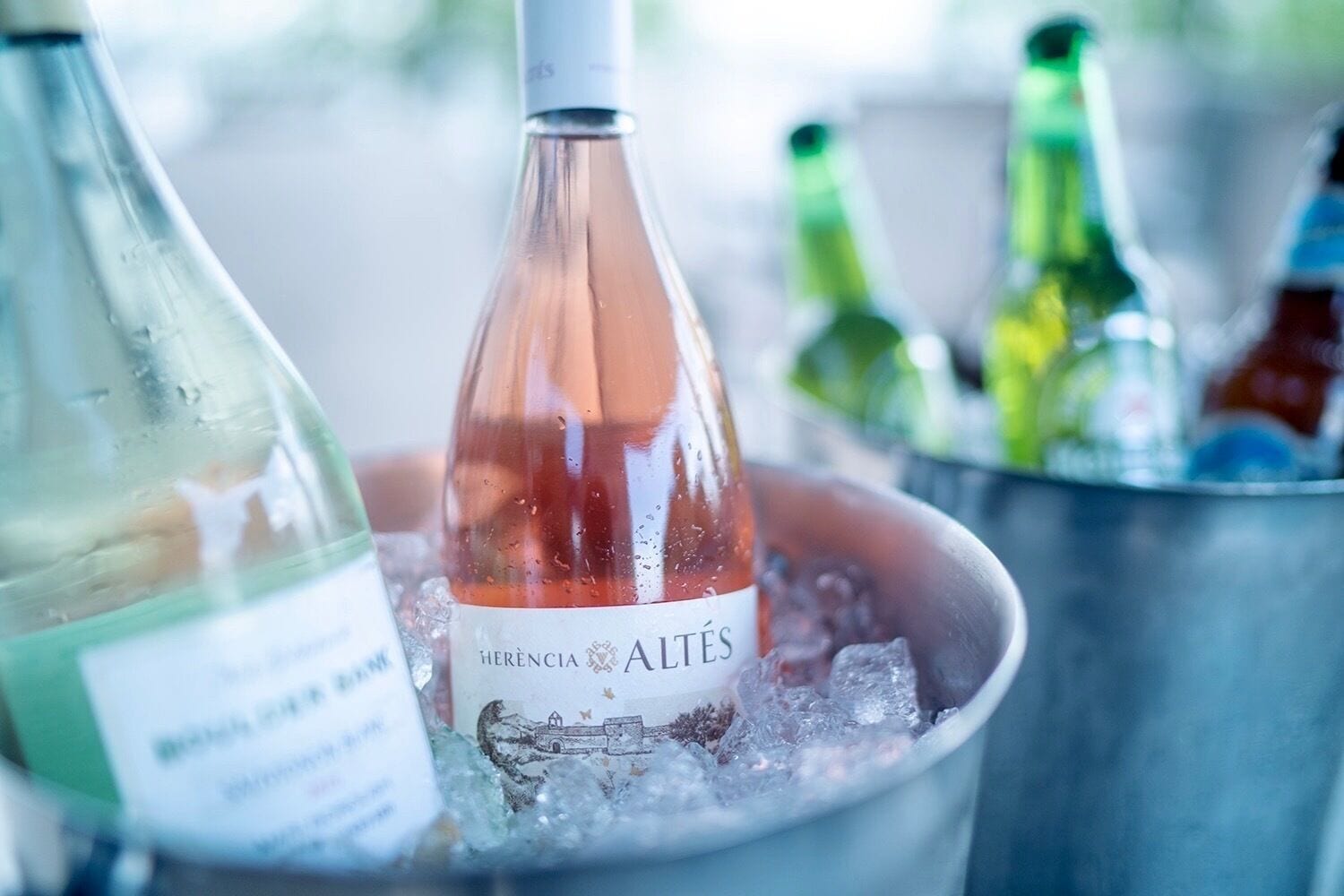 Ein mit Eis gefüllter Eimer mit Weinflaschen, darunter eine Flasche mit dem Aufdruck "HERENCIA ALTÉS".