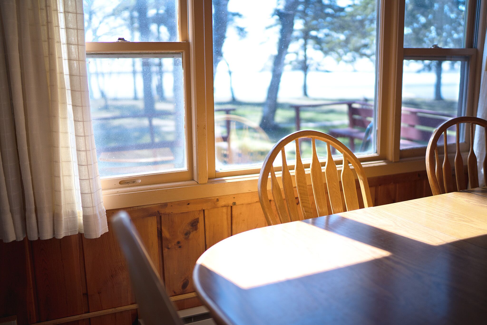 A dining table with wooden chairs and a window with curtains.