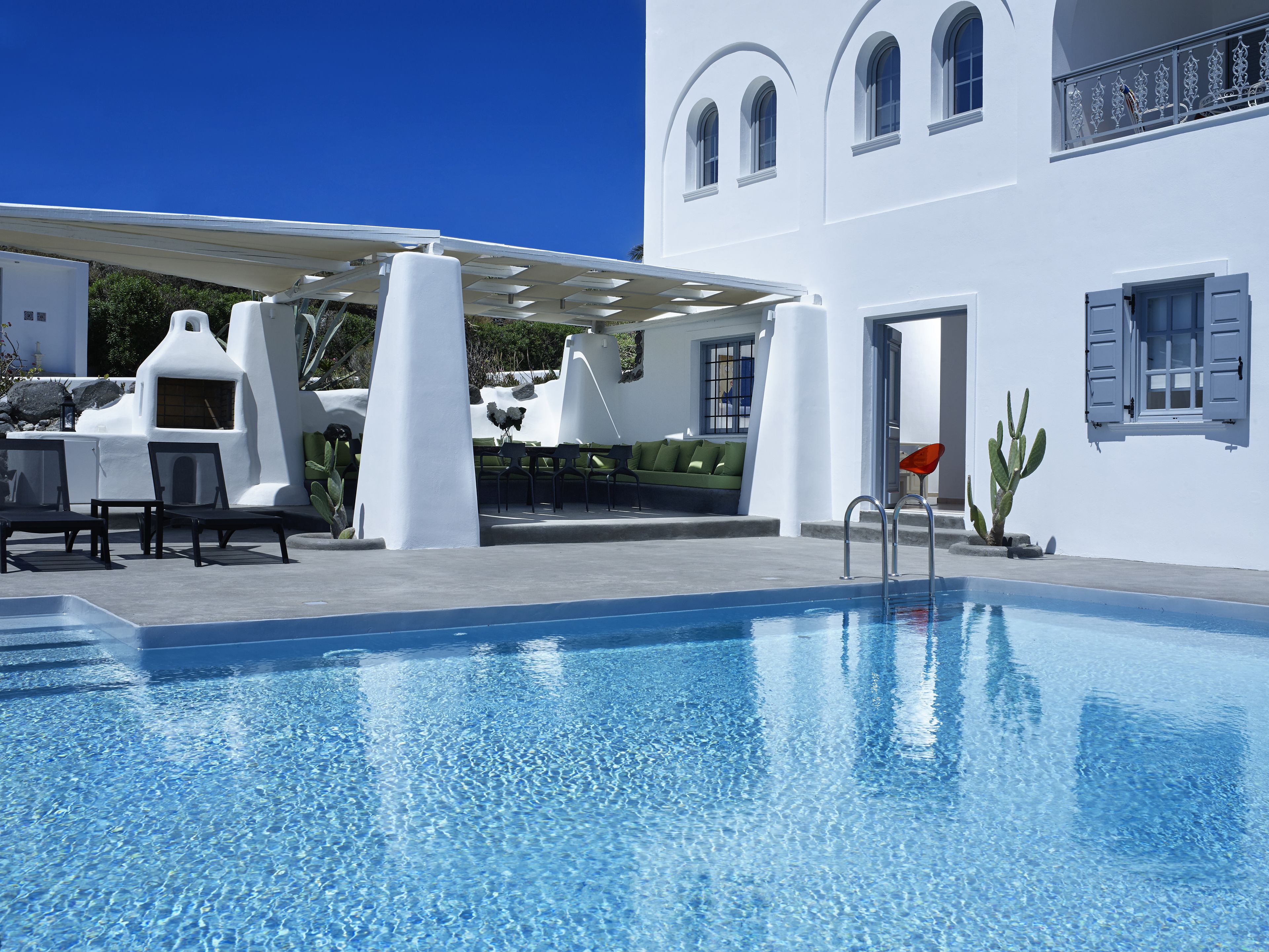 Un espace piscine doté d’une piscine à l’eau cristalline, de murs blancs et d’un coin salon abrité avec des chaises et une table.