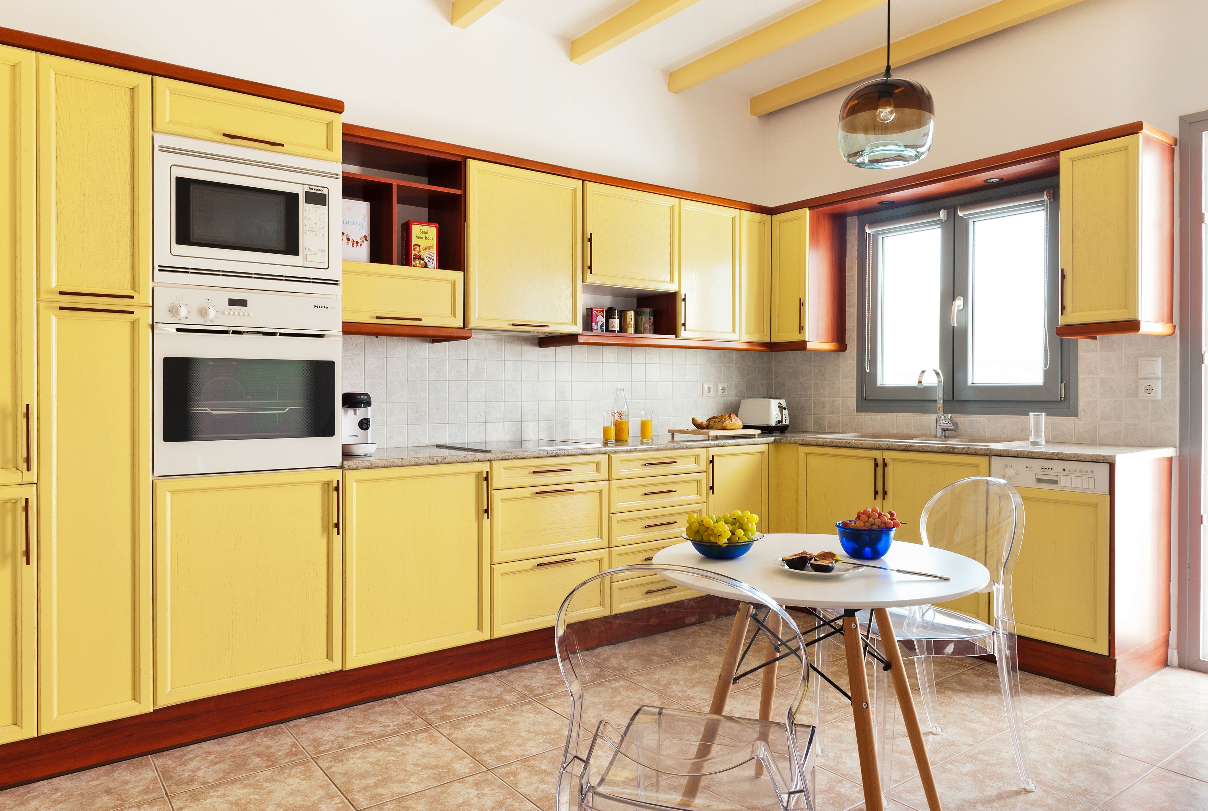 A kitchen with yellow cabinets, a white stove, and a dining area with a clear glass table.