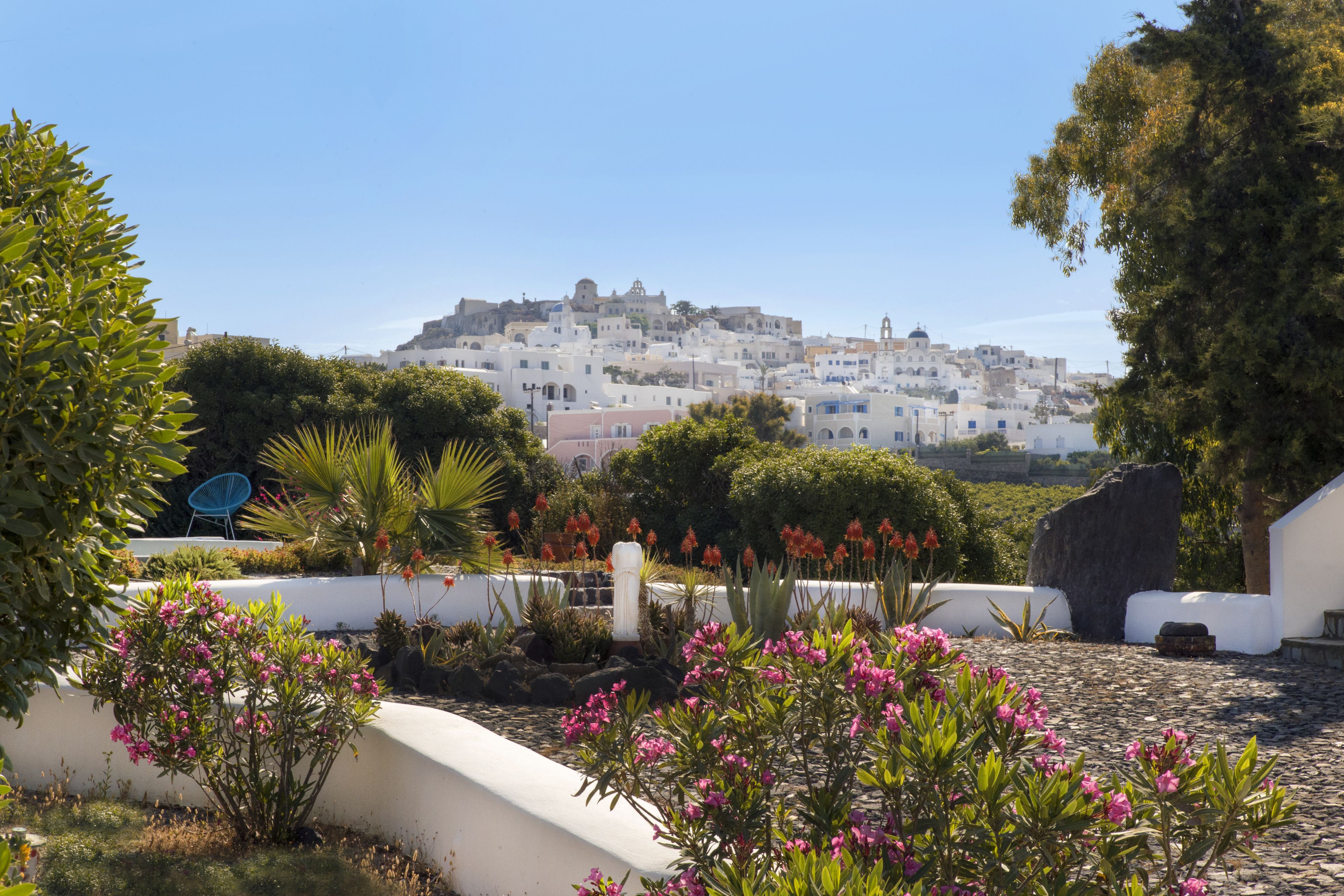 A courtyard with a white wall, a large rock, and pink flowers.