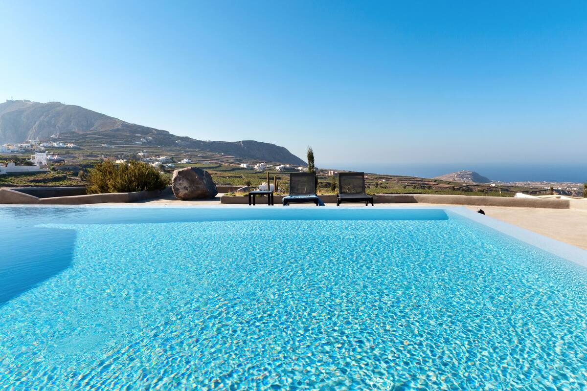 A clear blue pool with lounge chairs and a view of the sea and mountains.