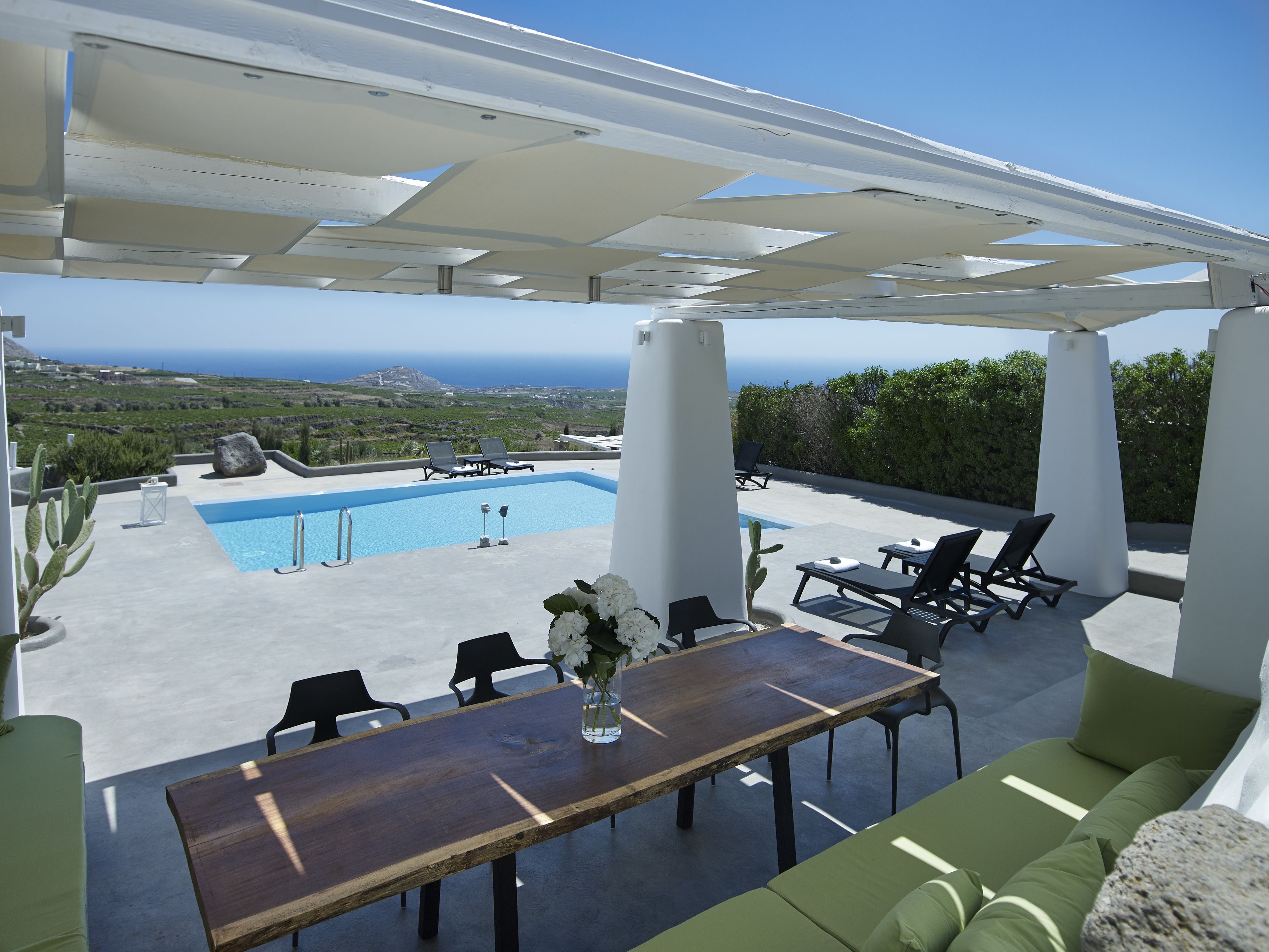 Un espace piscine aménagé sur le toit, offrant une vue sur la mer, avec une table en bois et des chaises longues.
