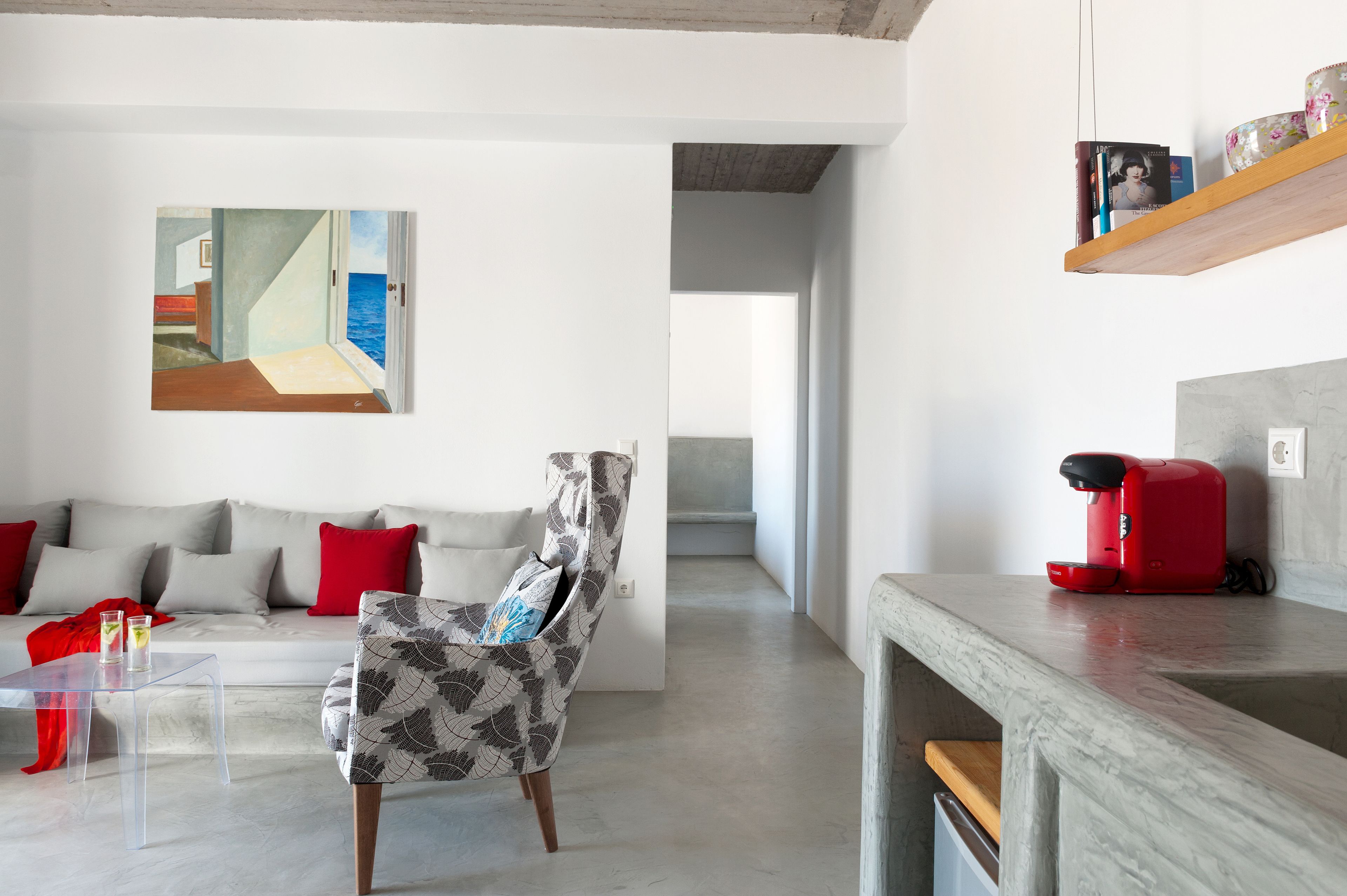 A modern living room with a sofa, a patterned armchair, a coffee machine, and a painting on the wall.