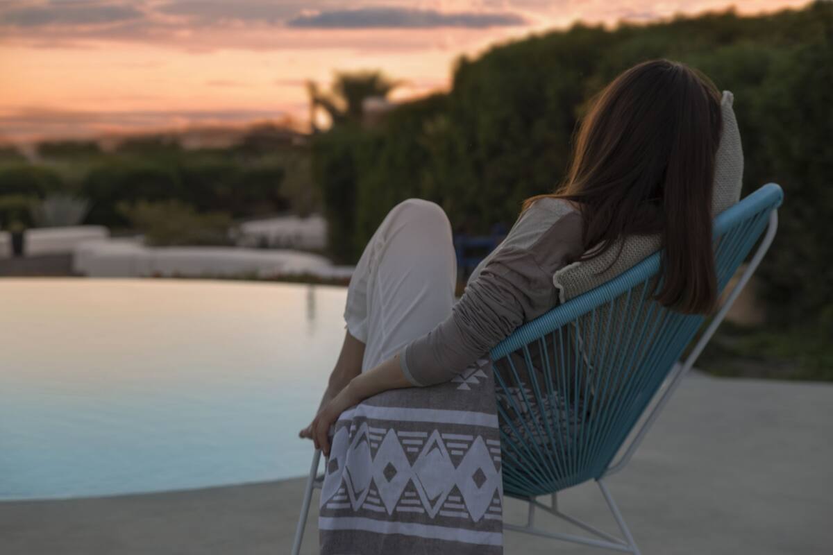 A person sitting on a chair by a pool with a patterned towel.