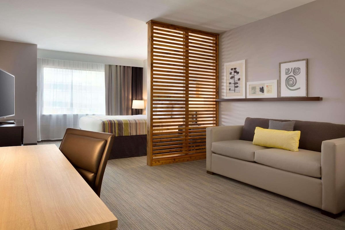A hotel room with a wooden partition, a sofa, a bed, a TV, and artwork on the wall.