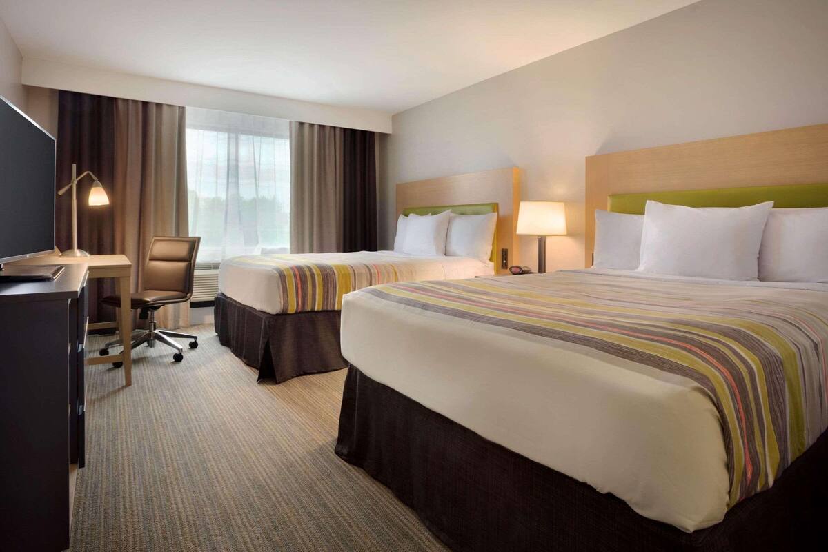 A hotel room with two beds, a desk, and a chair.