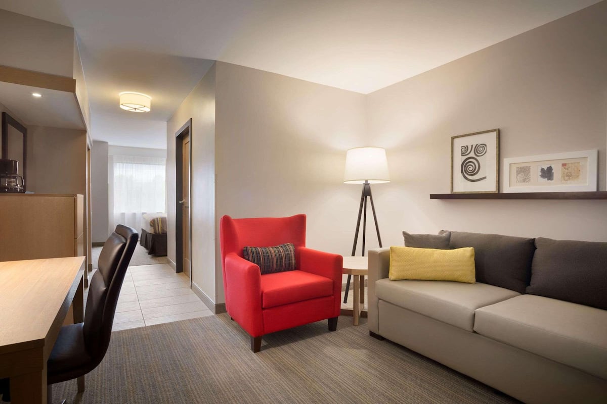 A hotel room with a red armchair, a beige sofa, a floor lamp, and a small table.