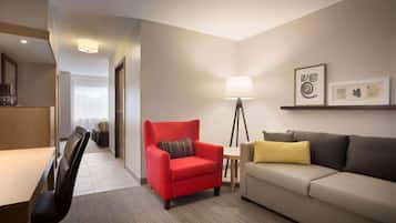 A hotel room with a red armchair, a beige sofa, a floor lamp, and a small table.