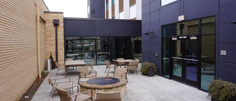 An outdoor patio area with tables and chairs, a fire pit, and a glass door entrance.