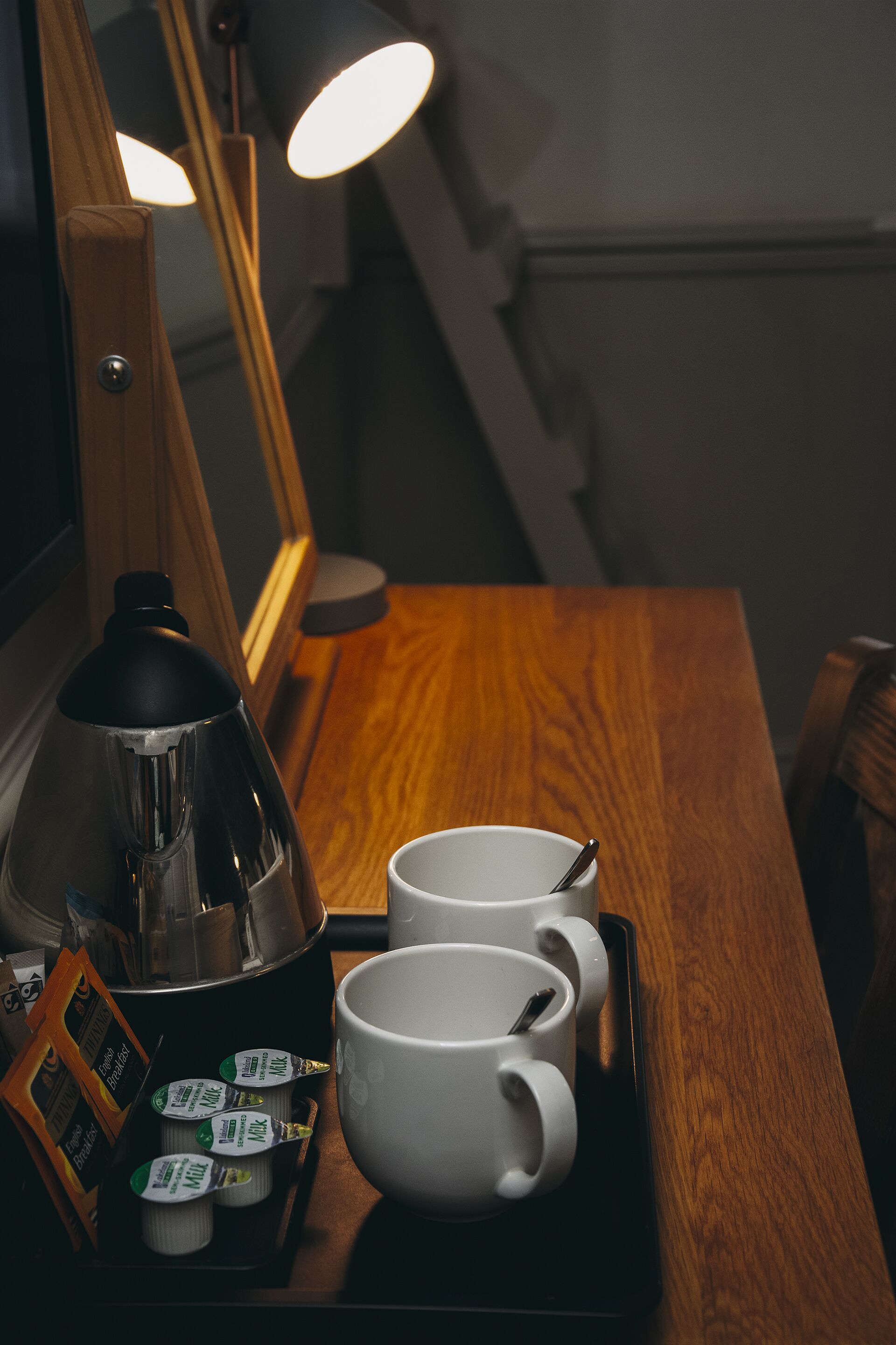 A wooden table with a coffee maker, two white cups, and a tray.