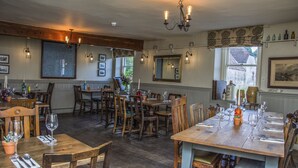 A dining area with wooden tables and chairs, chandeliers, and framed pictures on the walls. - The George Inn (Warminster)