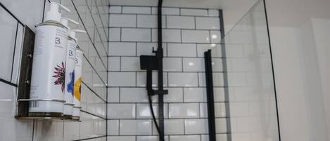 A bathroom with white tiled walls, a shower area, and a bottle of body wash on the wall.