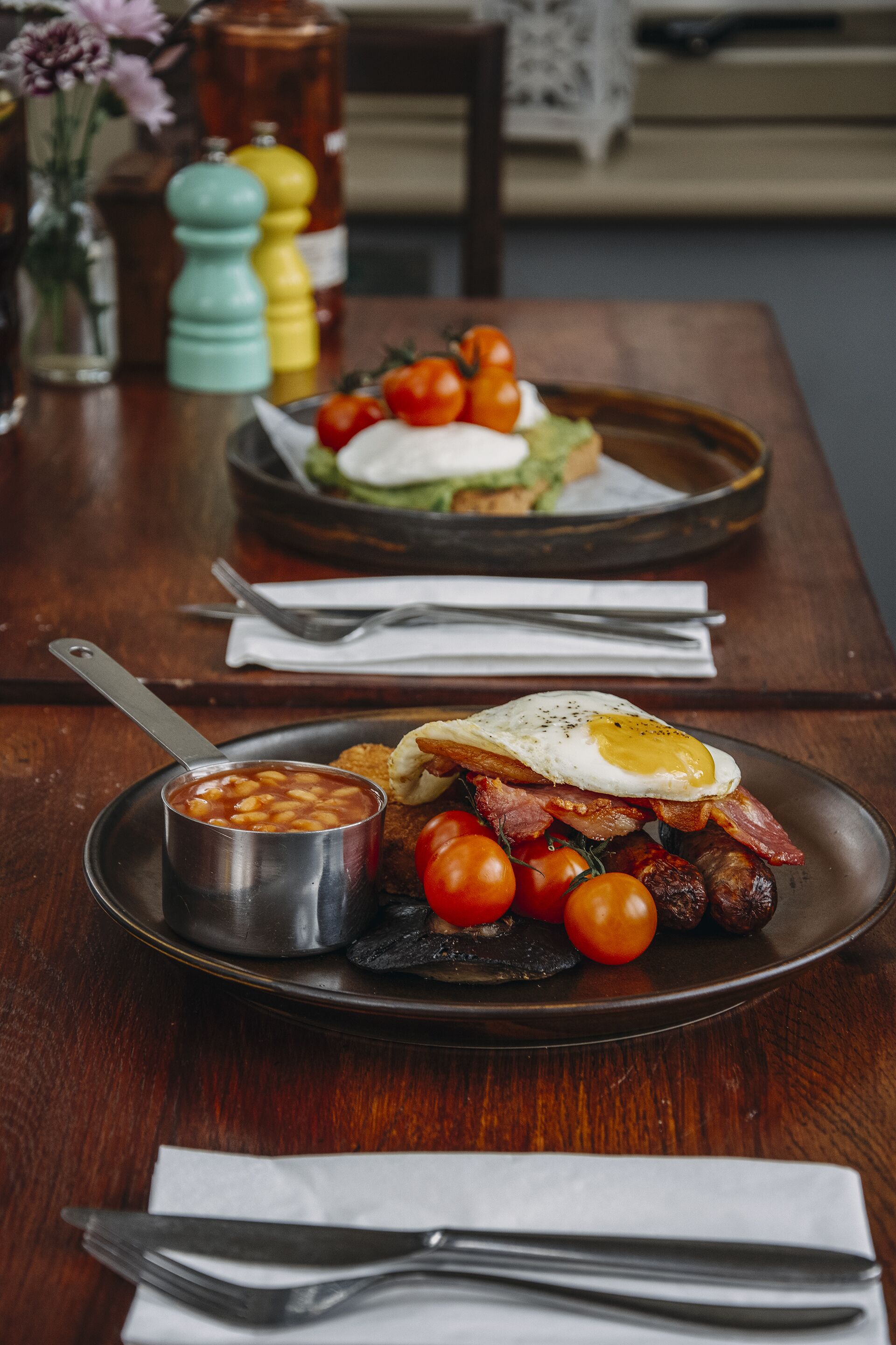A breakfast plate with eggs, bacon, beans, and tomatoes on a wooden table.