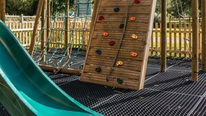 A playground with a slide, climbing wall, and wooden play structures. - The George Inn (Warminster)