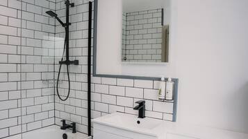A modern bathroom with white subway tiles, a black showerhead, a white sink, and a mirror above the mirror cabinet.