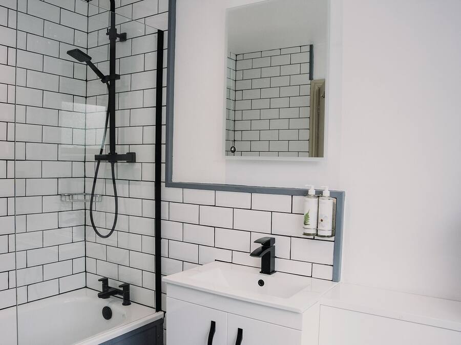 A modern bathroom with white subway tiles, a black showerhead, a white sink, and a mirror above the mirror cabinet.