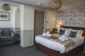 A bedroom with a bed, a chair, a door, and a wall with a patterned wallpaper.
