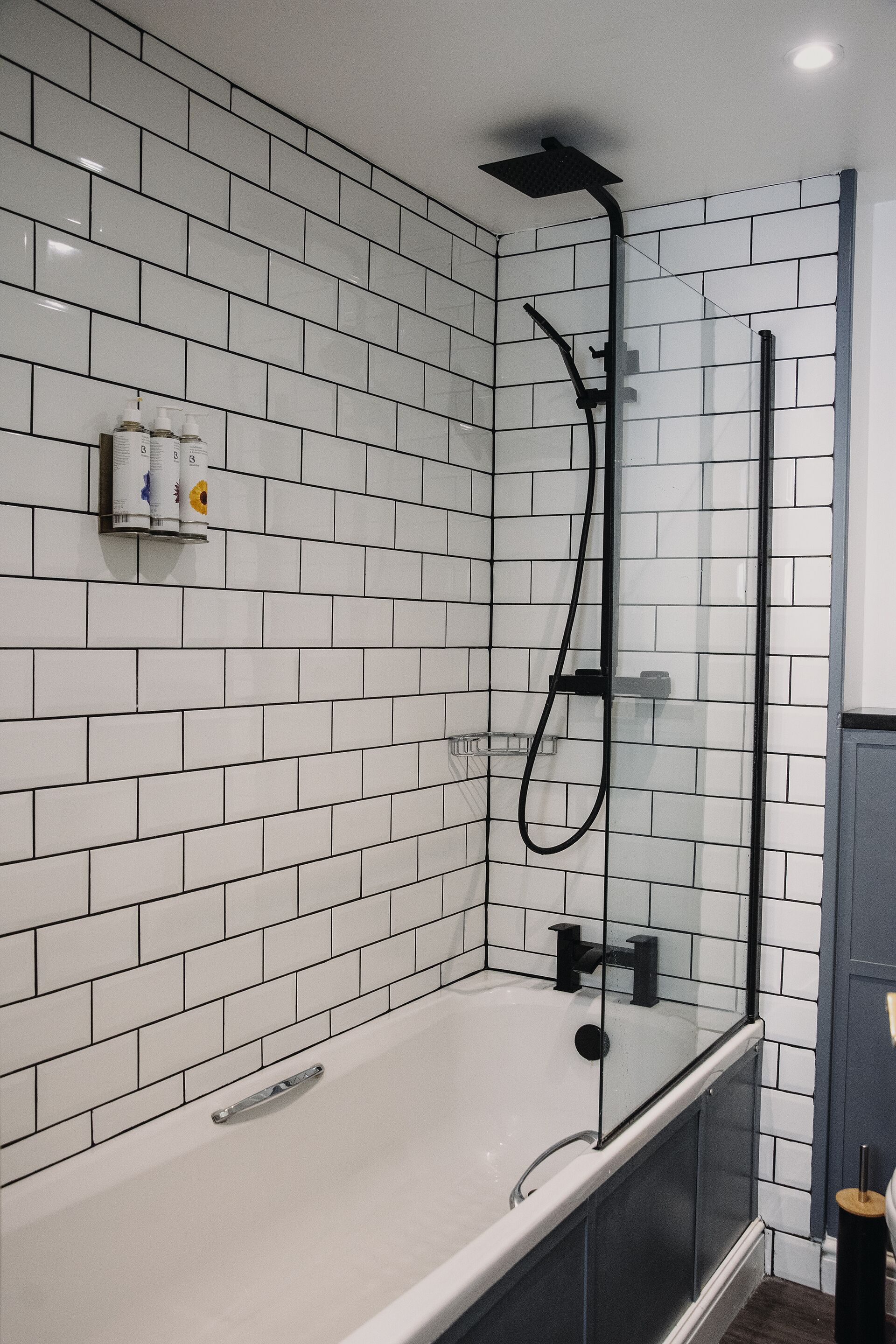 Une salle de bain moderne avec des carreaux de céramique blancs rectangulaires, une douche à parois de verre et une baignoire blanche.